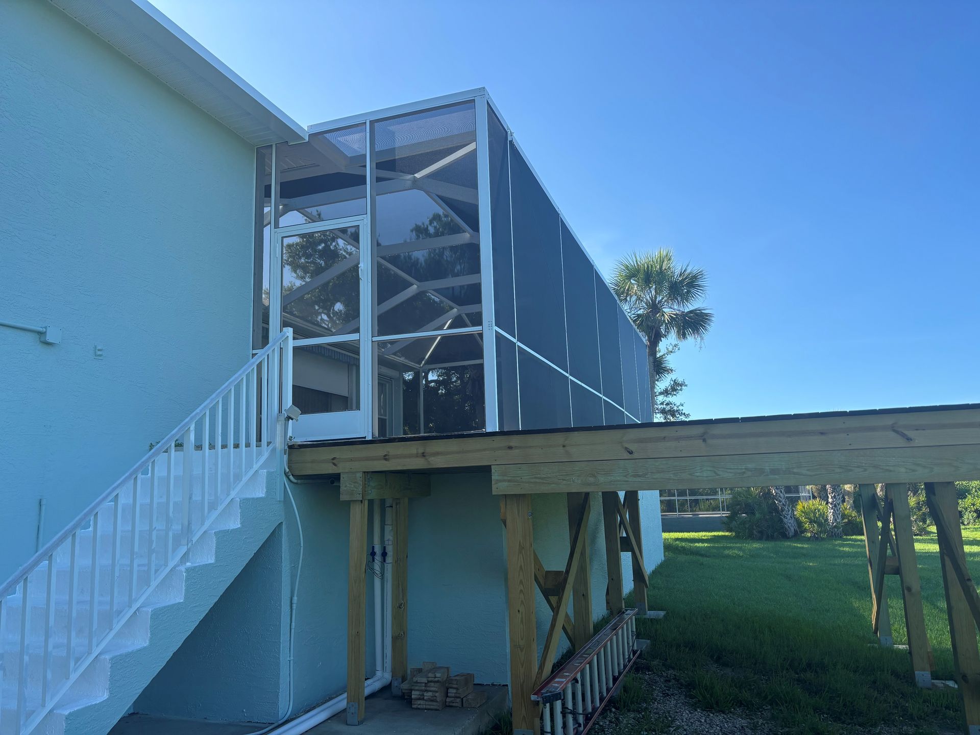 Screened porch attached to a light blue house with white stairs, wooden deck, and green grass.