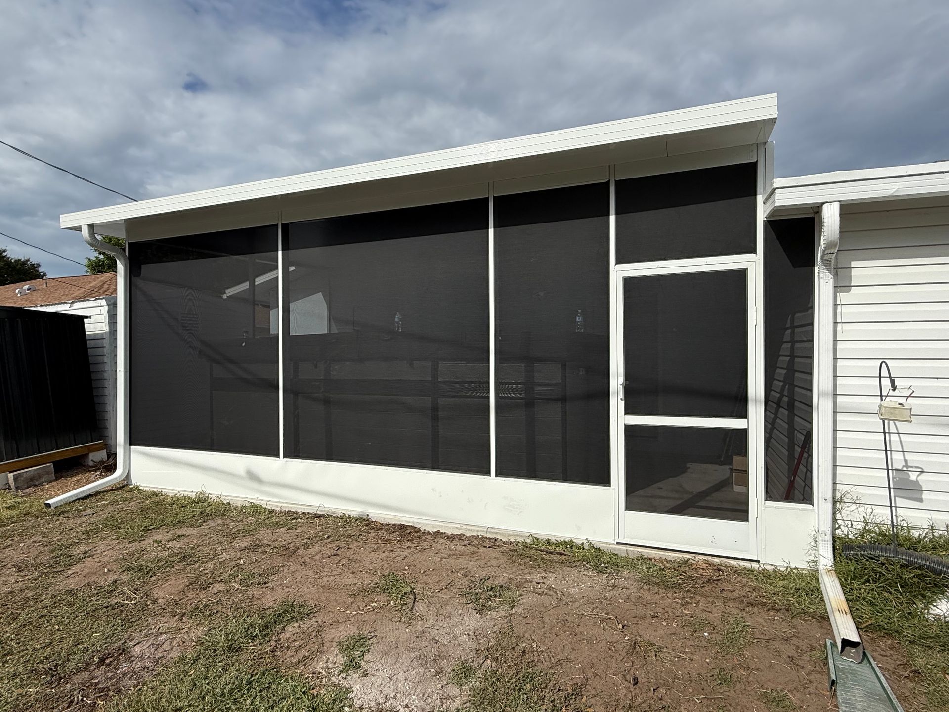 White screened-in porch with door attached to a house; black screens; overcast day.