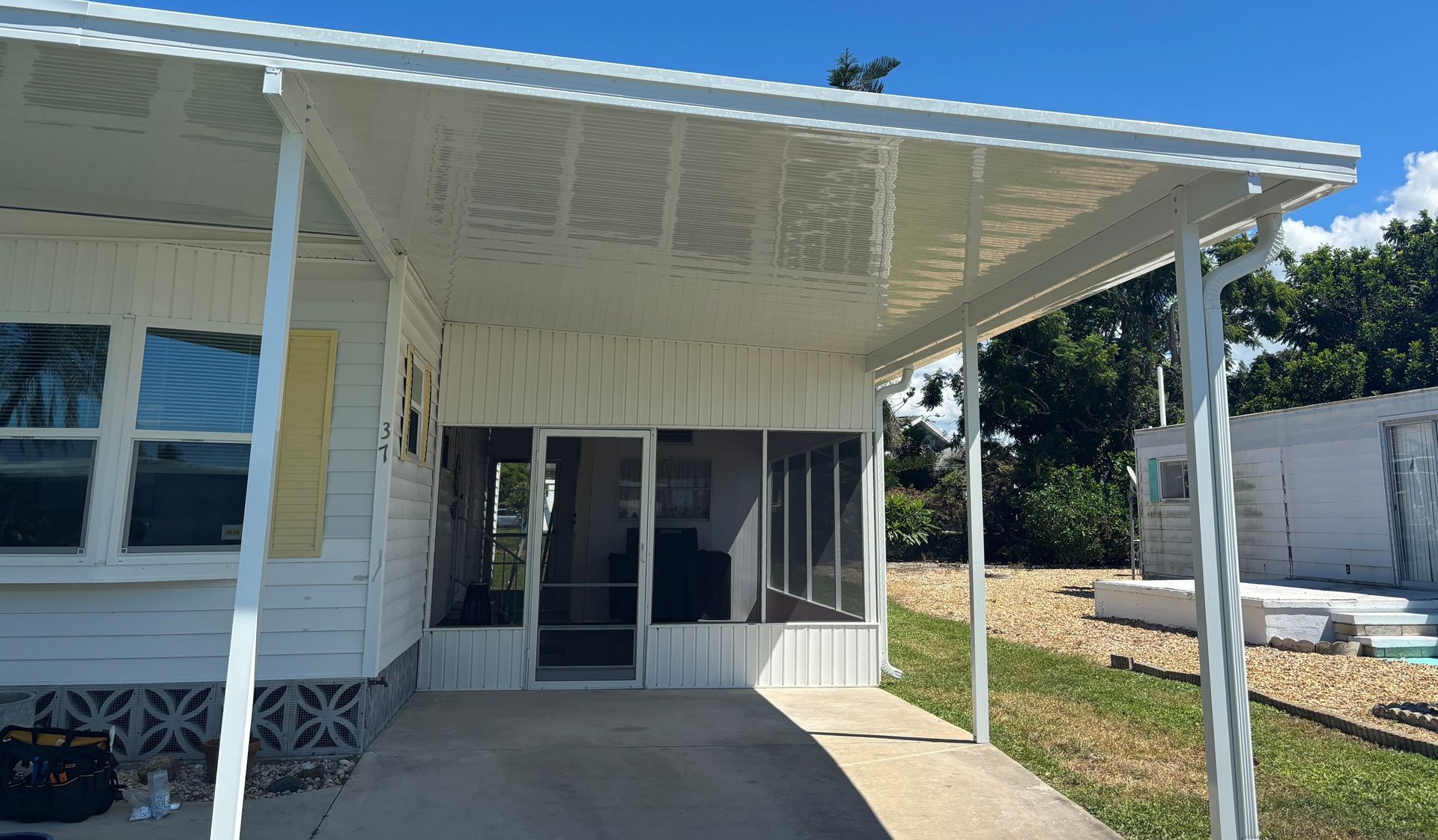 White awning over a porch with screen door, attached to a light-colored building with a blue sky in the background.
