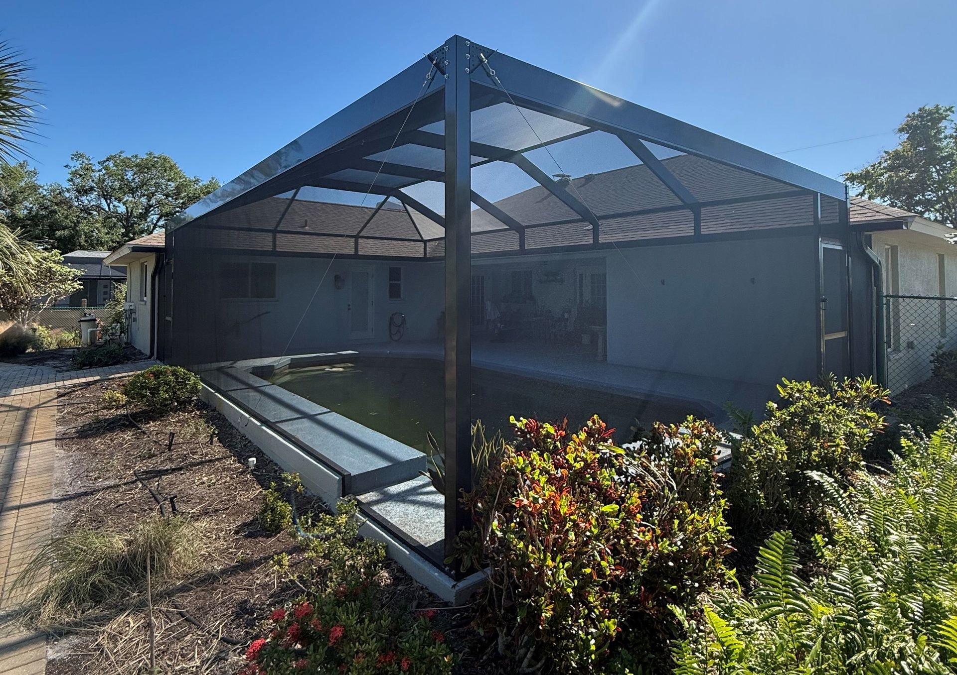 Pool enclosure with black frame and screened walls, protecting a pool and patio area.