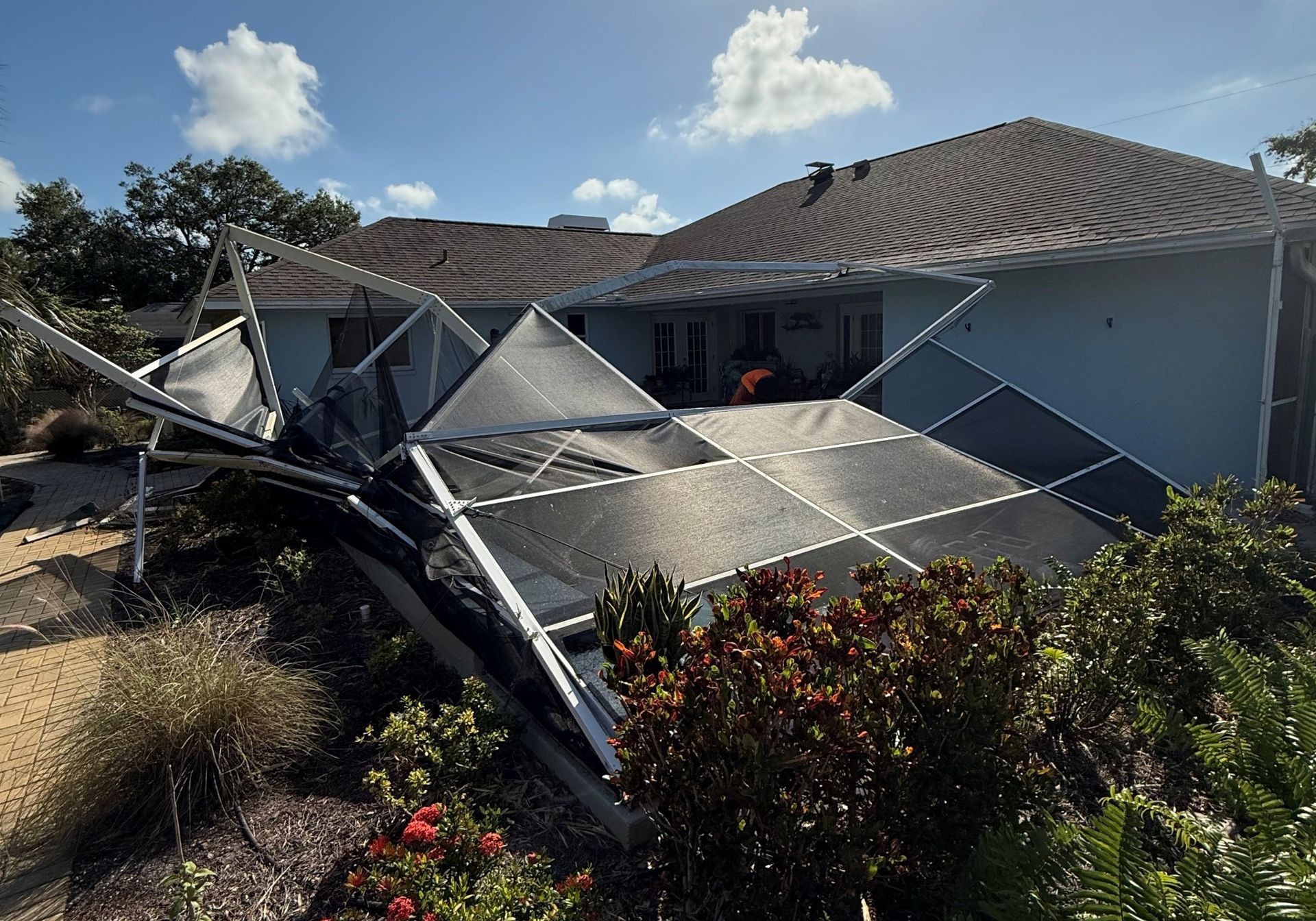 Collapsed pool enclosure next to a blue house with a dark roof on a sunny day.