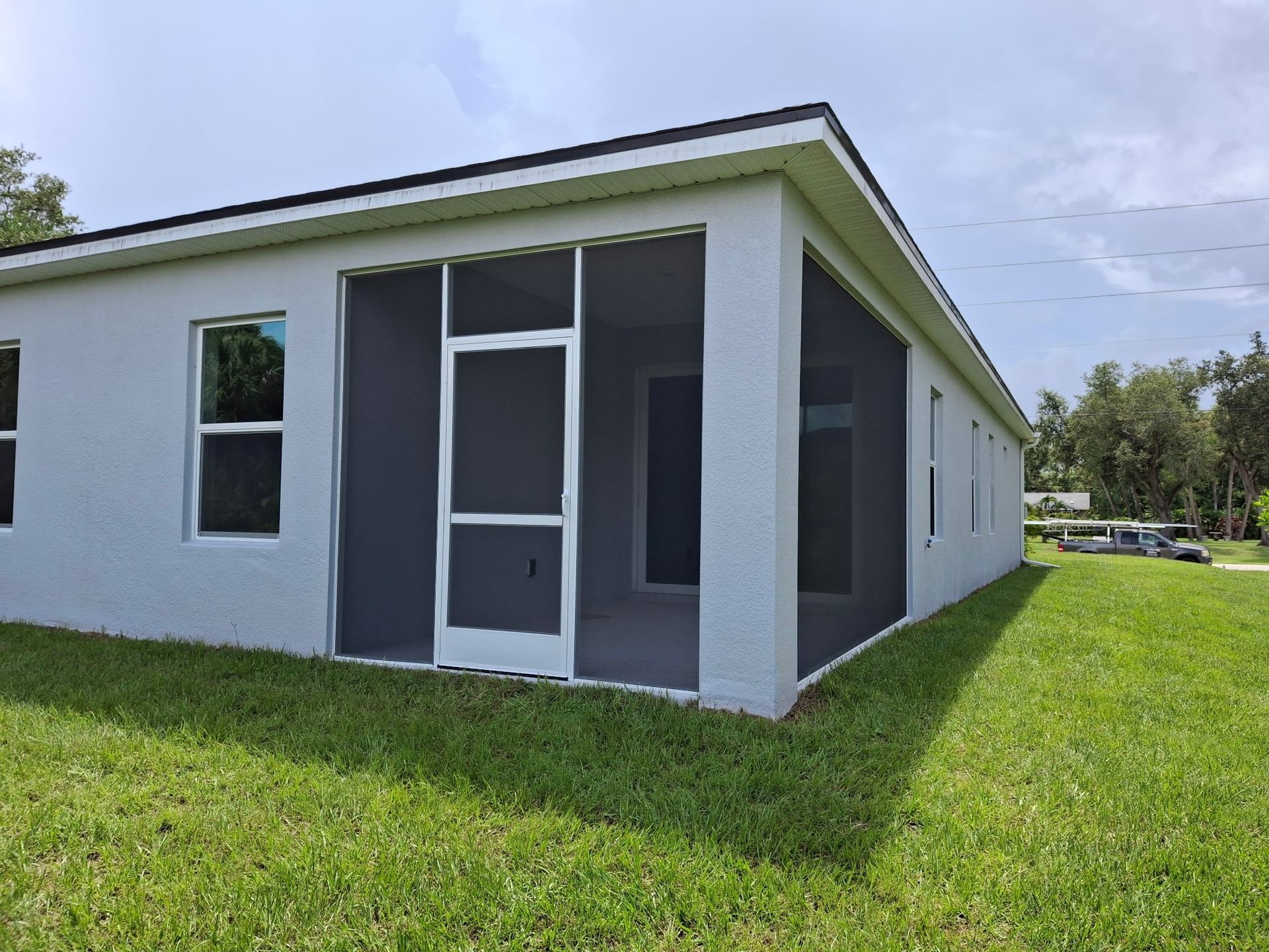 Light blue stucco house with screened-in porch and green lawn under a partly cloudy sky.
