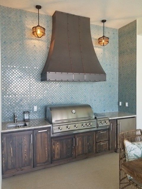 Outdoor kitchen with a stainless steel grill, copper range hood, and blue mosaic tile backsplash.