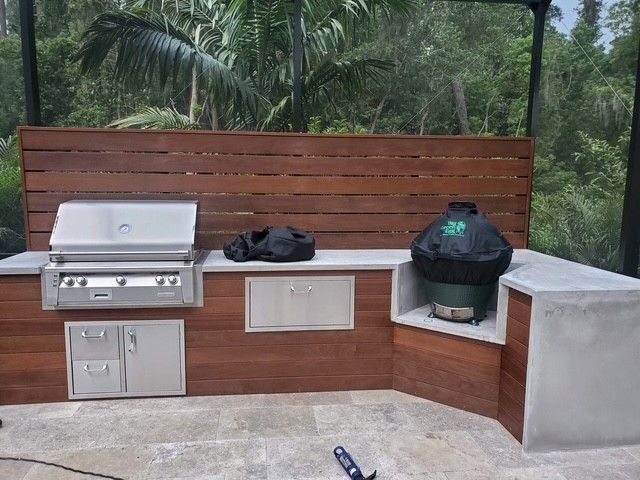Outdoor grilling station with stainless steel appliances, built-in Big Green Egg, and wood and concrete construction.