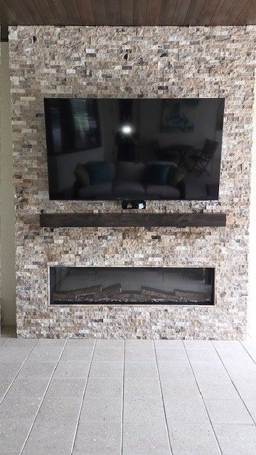 TV and fireplace set in a stone wall, dark wood shelf, gray tile floor.