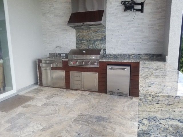 Outdoor kitchen with stainless steel appliances, granite countertops, and tiled walls and floor.