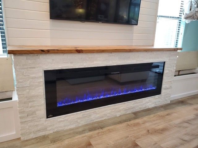 Electric fireplace with blue flame, framed by white stone, topped with a wood mantle and a mounted TV.