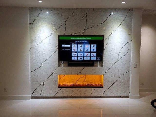 TV mounted above an electric fireplace on a marble-style wall with accent lighting.