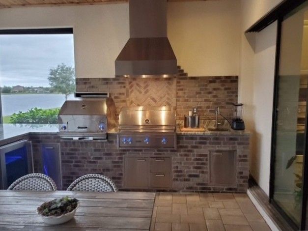Outdoor kitchen with brick, stainless steel appliances, and a lake view.