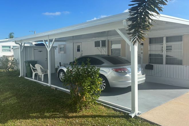 Car parked under a white carport next to a manufactured home on a sunny day.