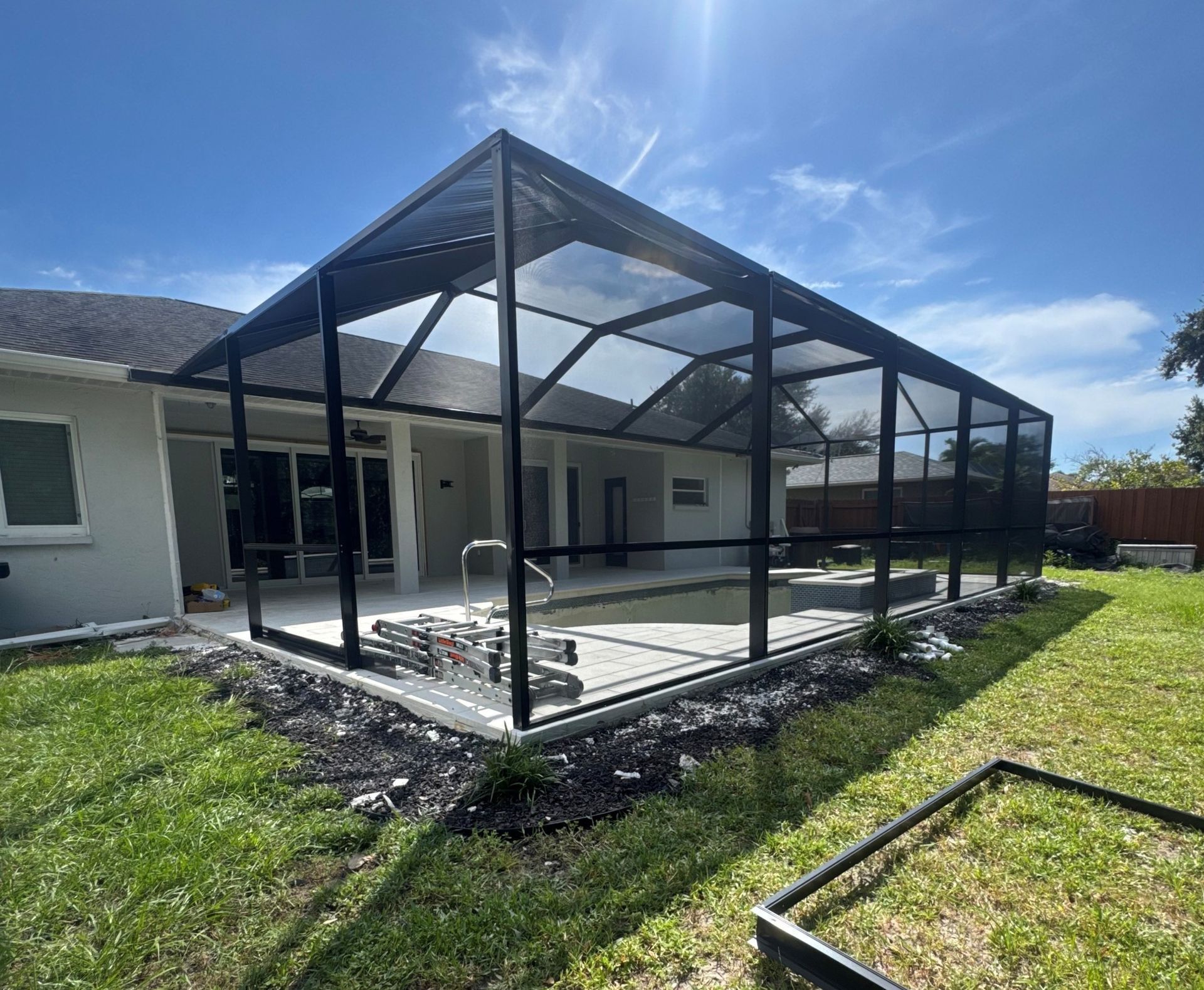 Woman in yellow shirt, sunglasses pressure washes white screened enclosure against a blue sky.