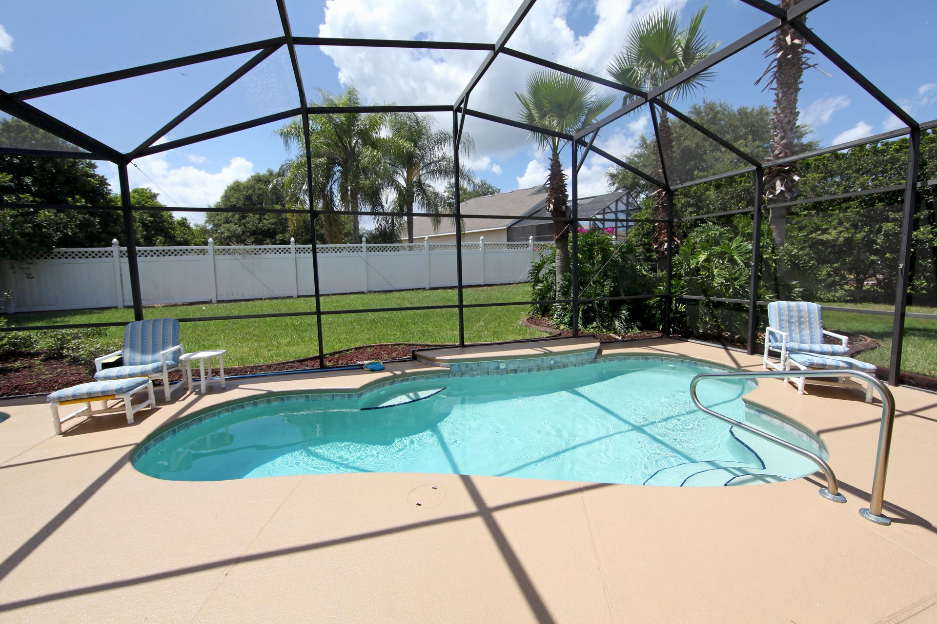 Swimming pool with screened enclosure, two lounge chairs, and palm trees.