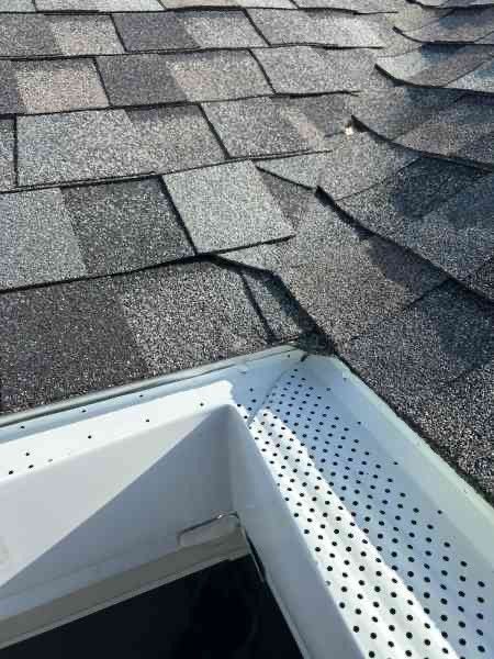 Patio with gray couch, wicker furniture, wood deck, and pergola, overlooking a lawn and a large house.