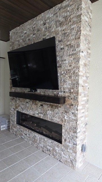 Bright sunroom with brick wall, skylights, and windows overlooking a yard, furnished with a table, sofa, and TV.