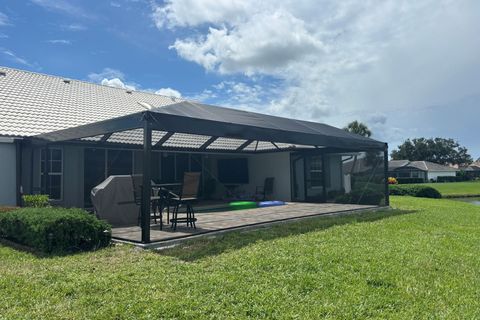 Patio with dark gray canopy attached to a house with a green lawn and cloudy sky.