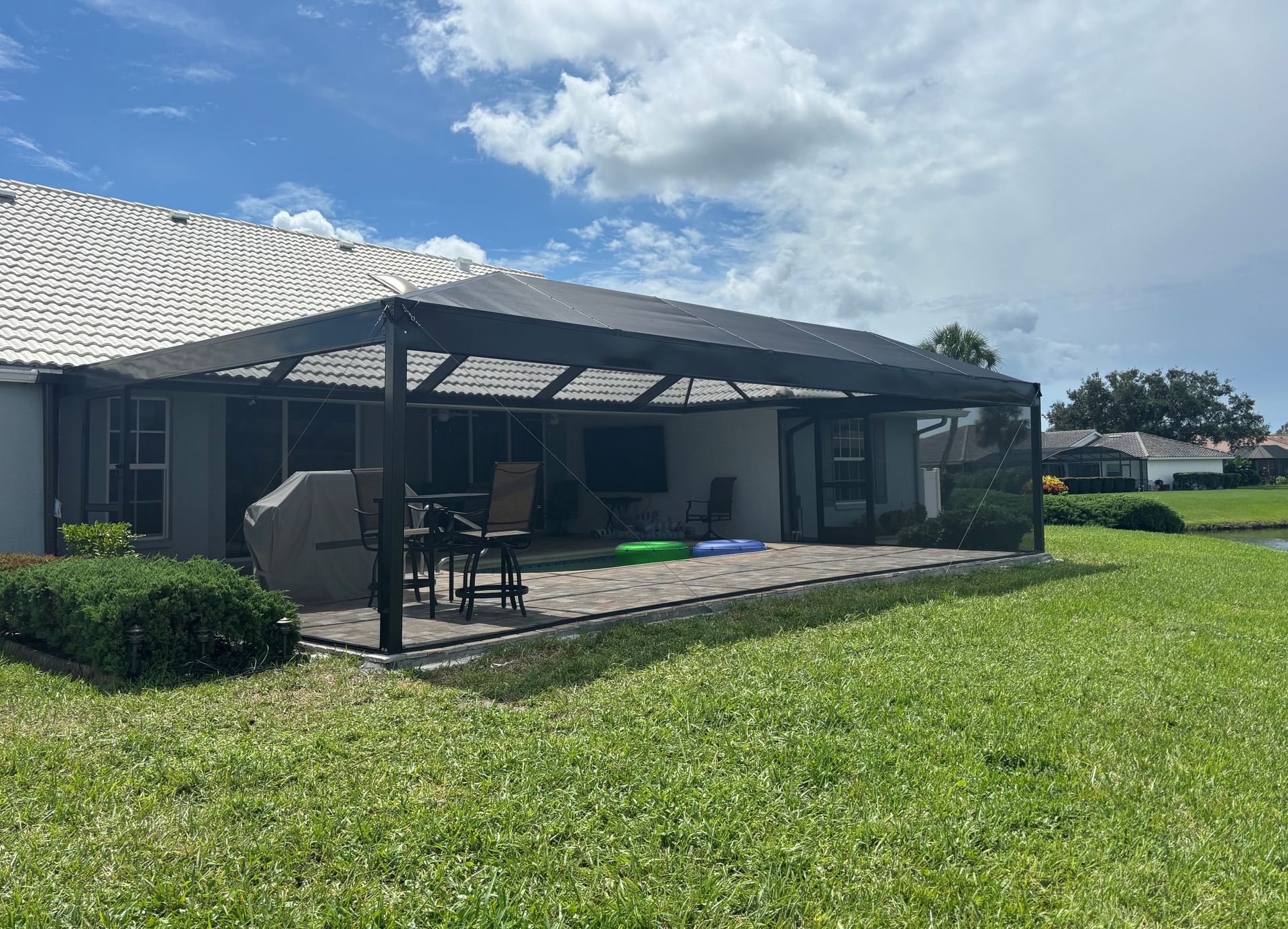 Patio with dark roof, barbecue, and lawn, under a partly cloudy sky.