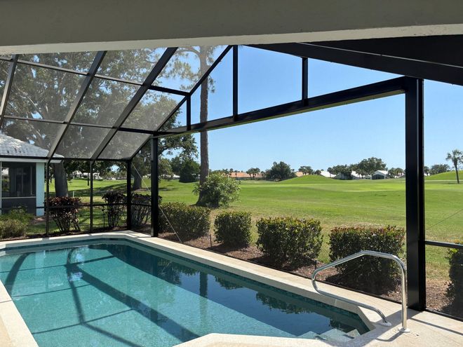 Pool and hot tub with waterfall feature, surrounded by lush landscaping and screened enclosure.