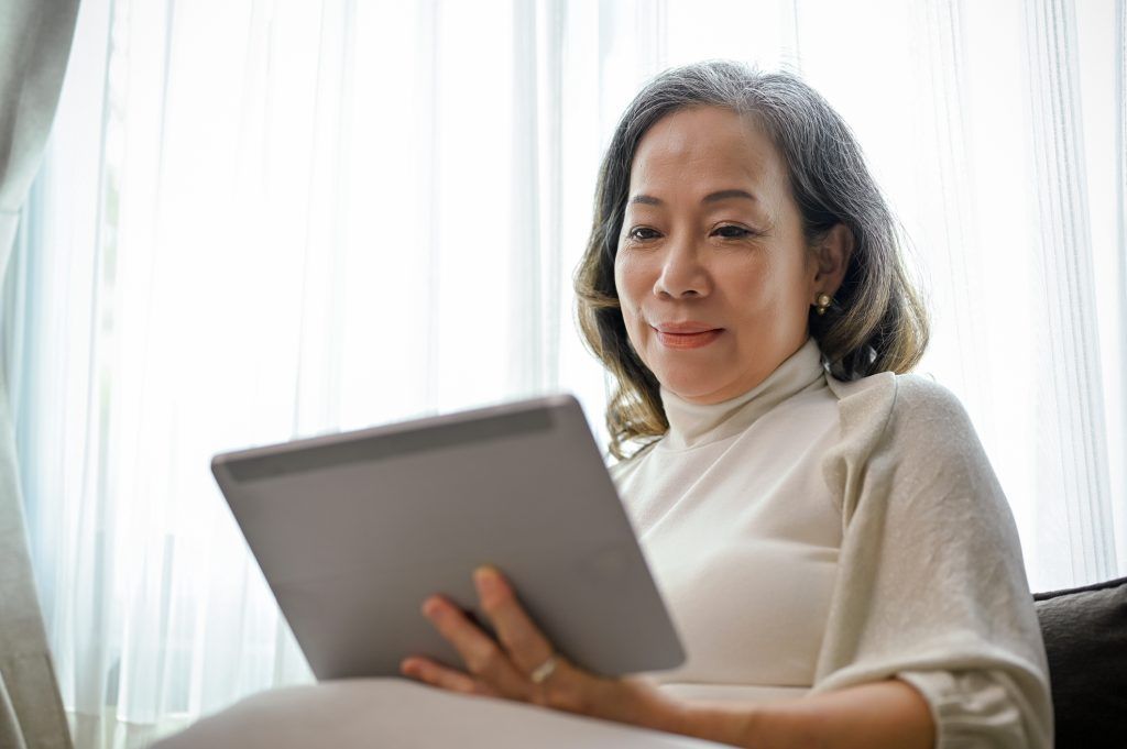 An older woman is sitting on a couch using a tablet computer.