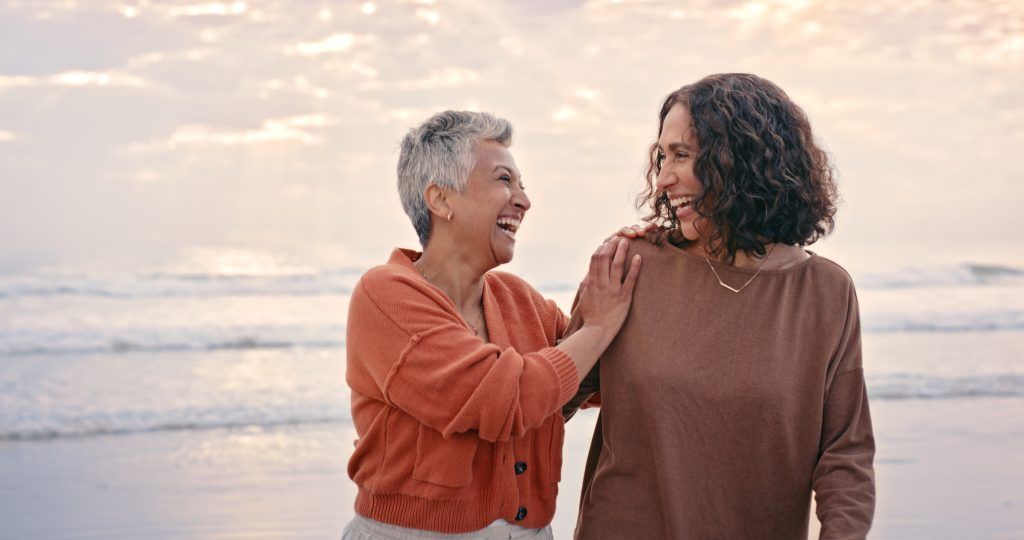 Two women are standing on the beach talking to each other.