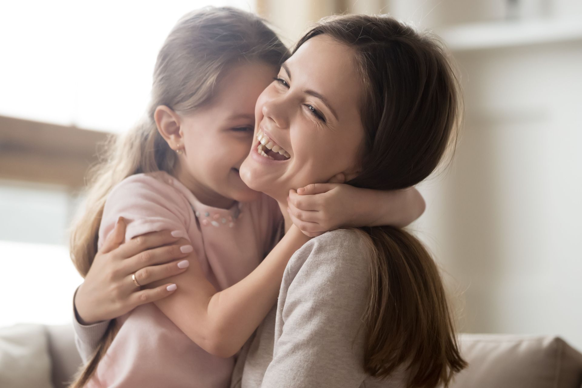 A woman and a little girl are hugging each other on a couch.