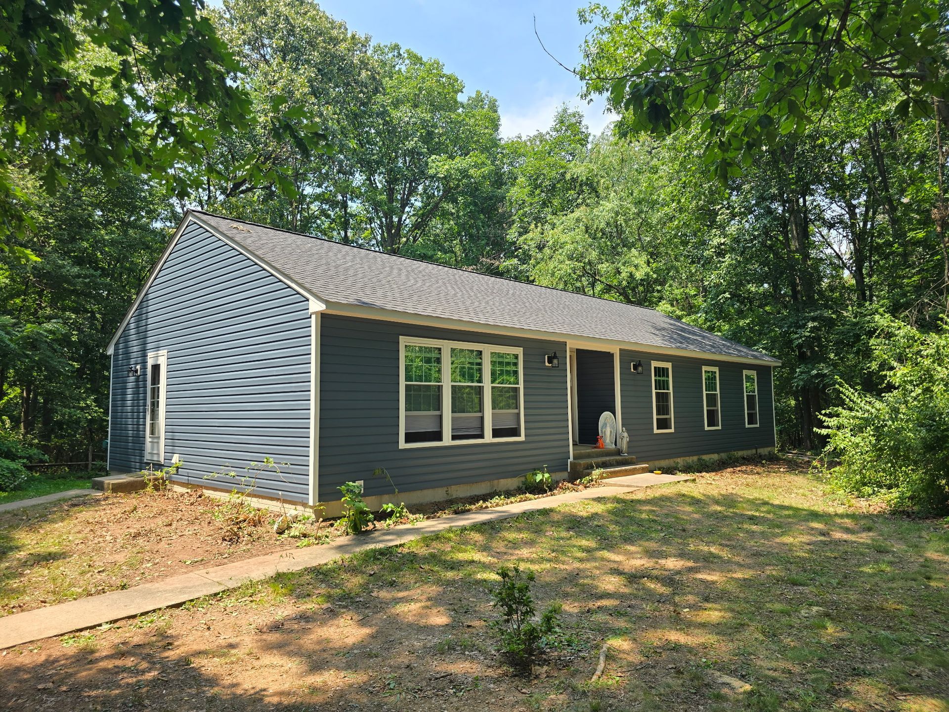 Gray house with white trim in a wooded clearing, viewed from the front-left side