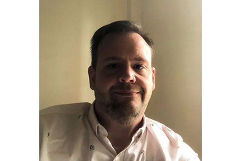 A man with a beard is smiling for the camera while wearing a white shirt.