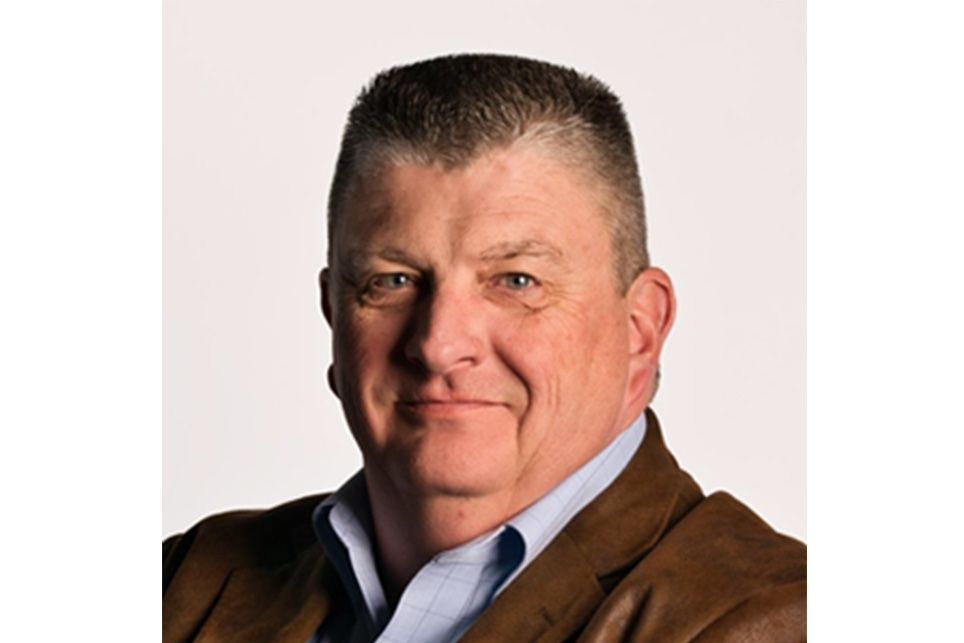 A man in a brown jacket and blue shirt is smiling for the camera.