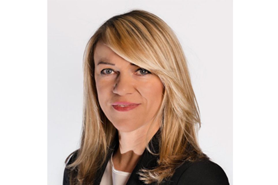 A woman with blonde hair and a black jacket is smiling for the camera.