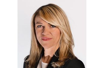 A woman with blonde hair and a black jacket is smiling for the camera.