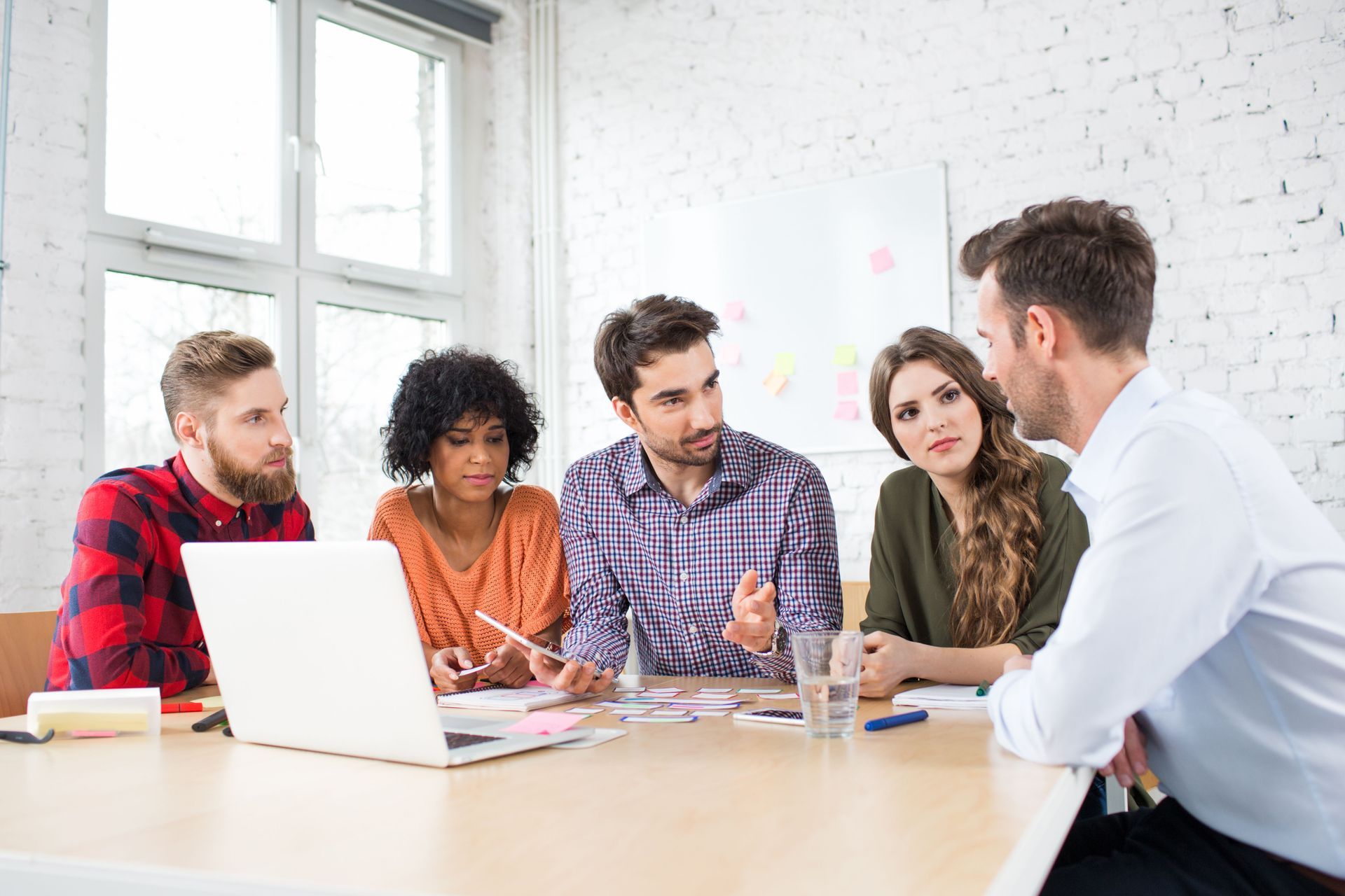 Five colleagues sit around a table in a bright office, looking at a laptop and discussing a project.