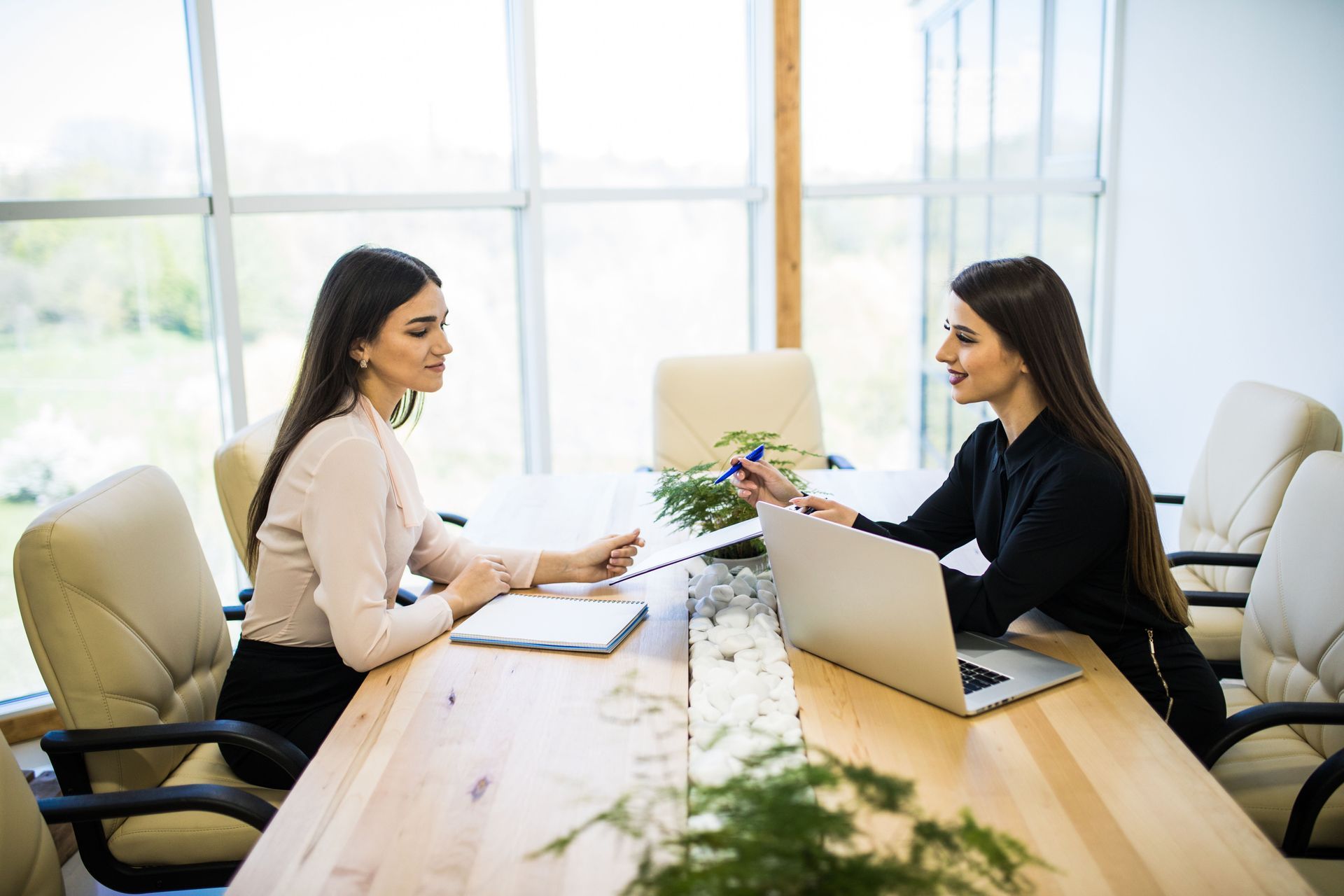 Two people in business attire sit across from each other at a wooden office desk, engaged in a professional discussion.