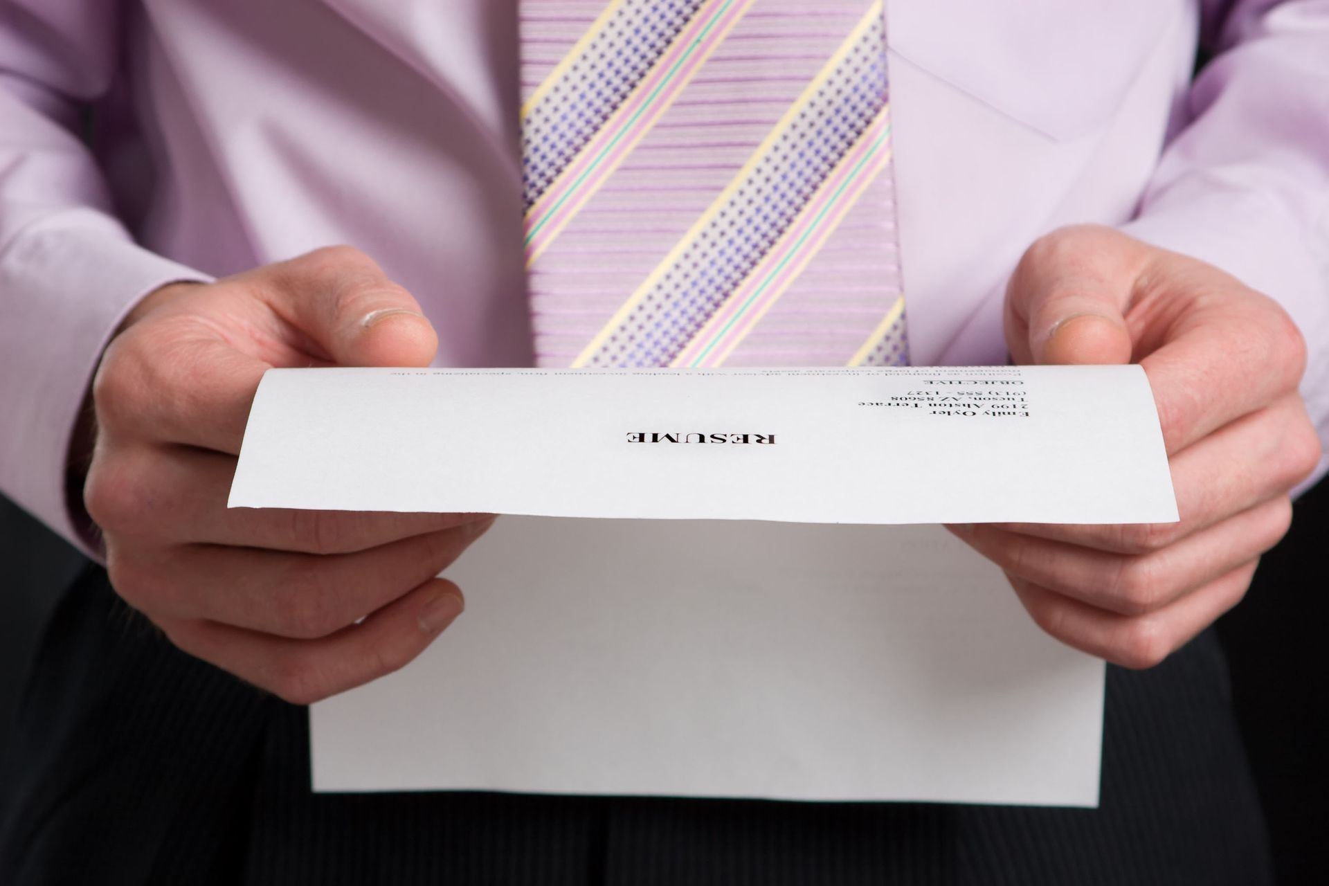 A close-up of a resume on a desk with a gold pen resting on it and reading glasses placed nearby.