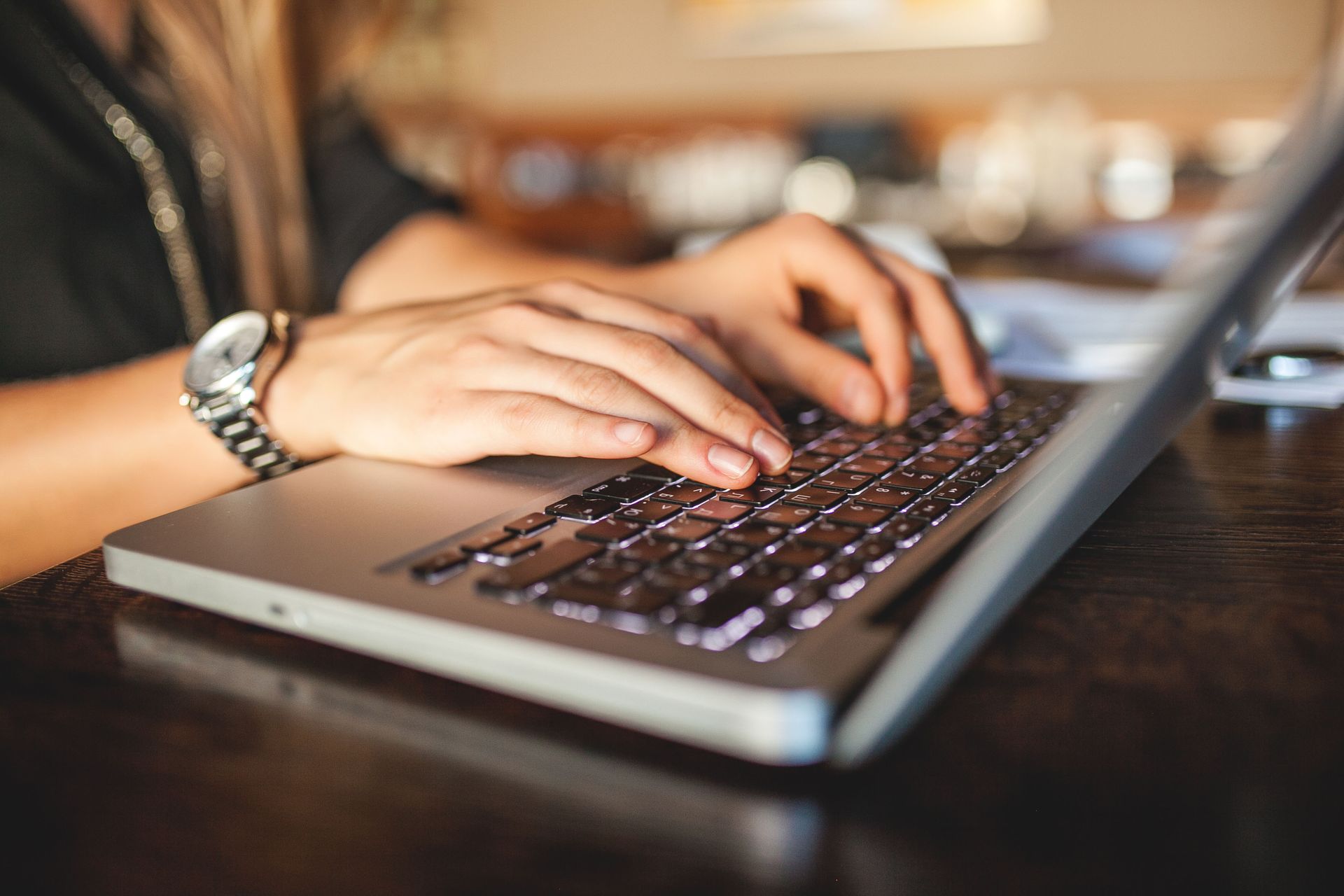 Close-up of hands typing on a laptop keyboard at a wooden desk.