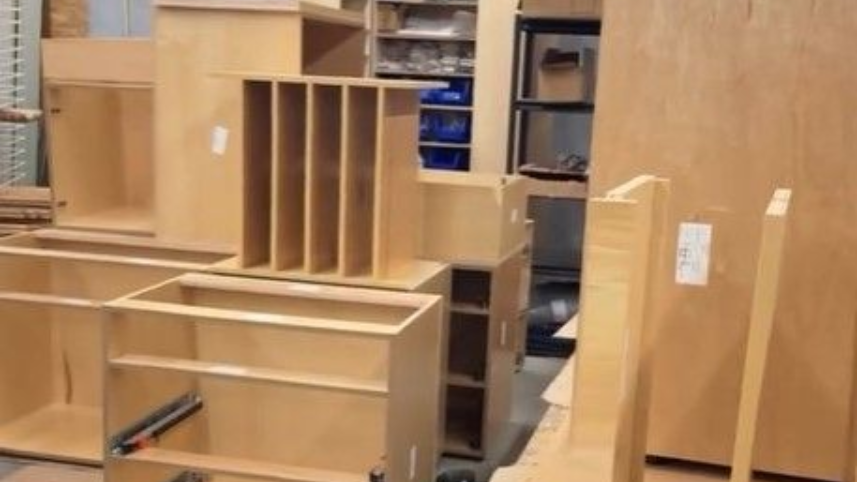 Wooden cabinets and shelving units in a workshop or storage area, unfinished furniture parts stacked inside.
