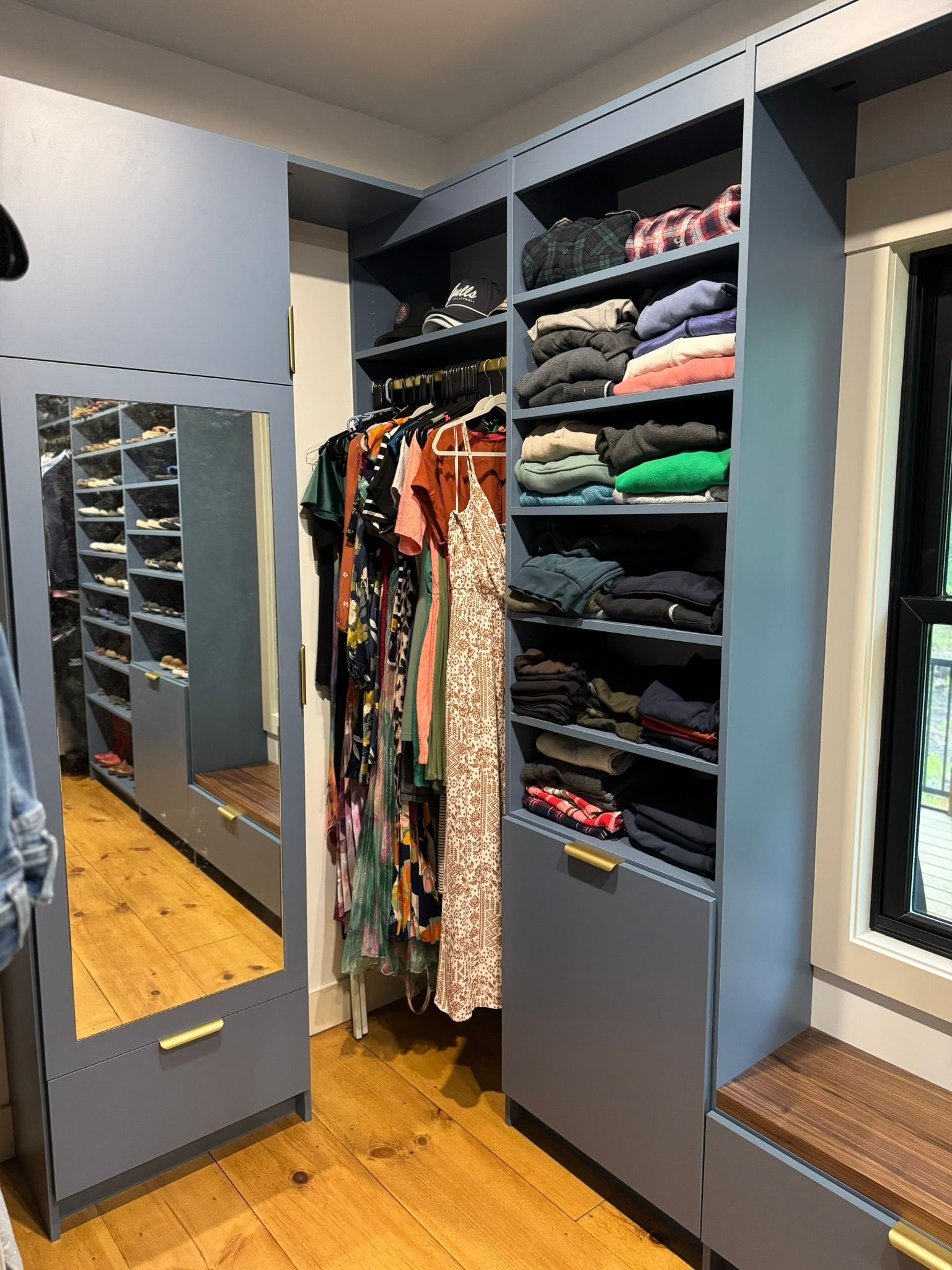 Walk-in closet with hanging clothes, folded shelves, and a full-length mirror on a wood floor