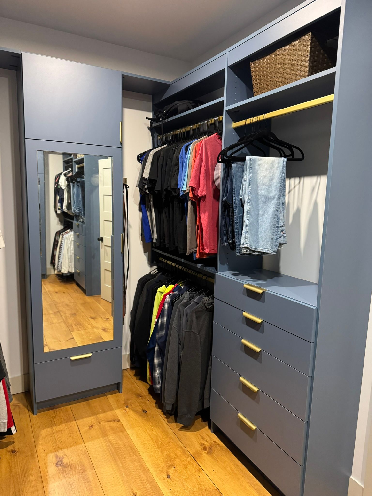 Walk-in closet with open shelving, hanging clothes, drawers, and a full-length mirror on a gray wall.