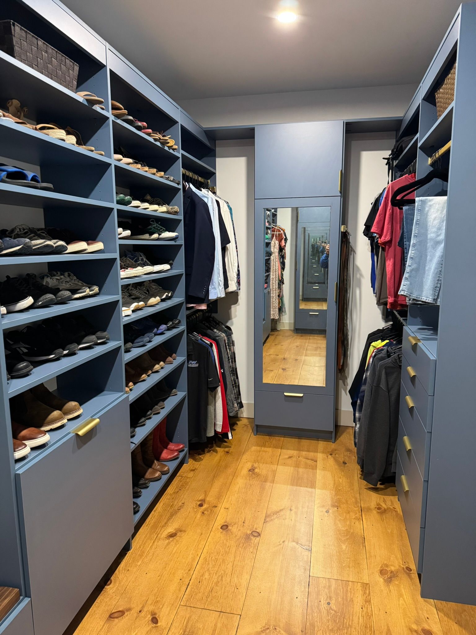Walk-in closet with blue shelves, hanging clothes, and a mirror over a wood floor.