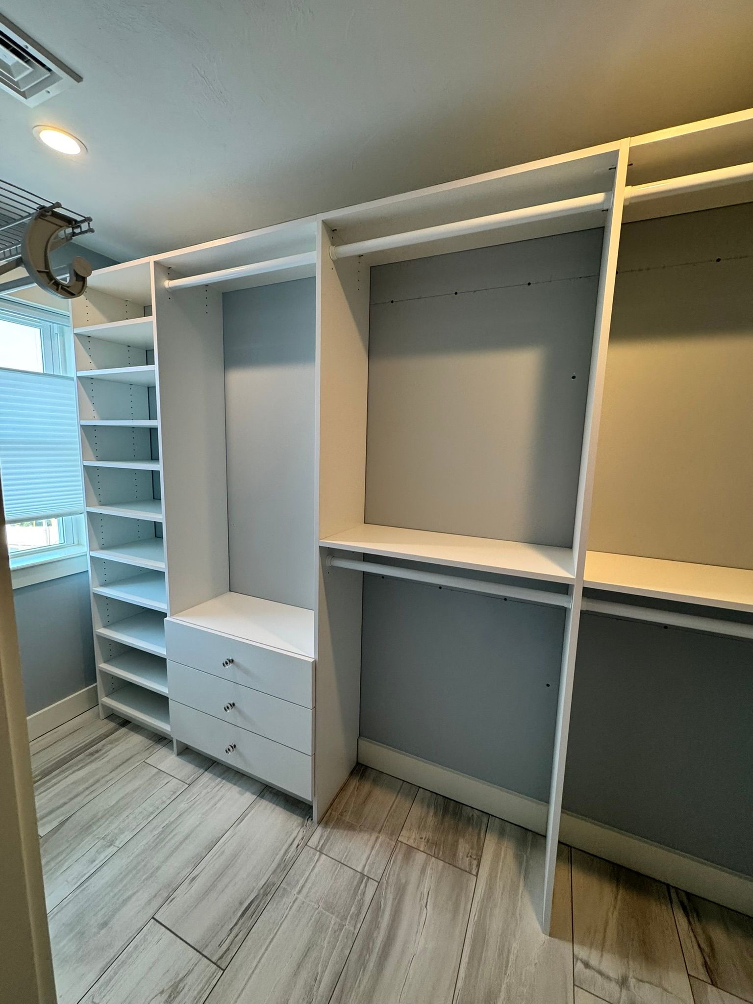 White built-in closet with shelves, drawers, and hanging sections in a light wood-floored bedroom.