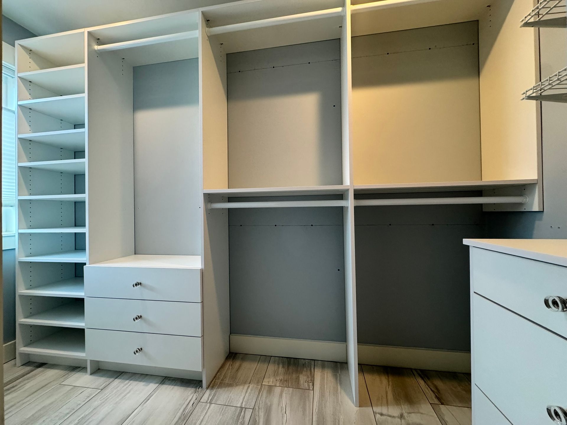 Empty white walk-in closet with shelves, hanging rods, and drawers on a light wood floor