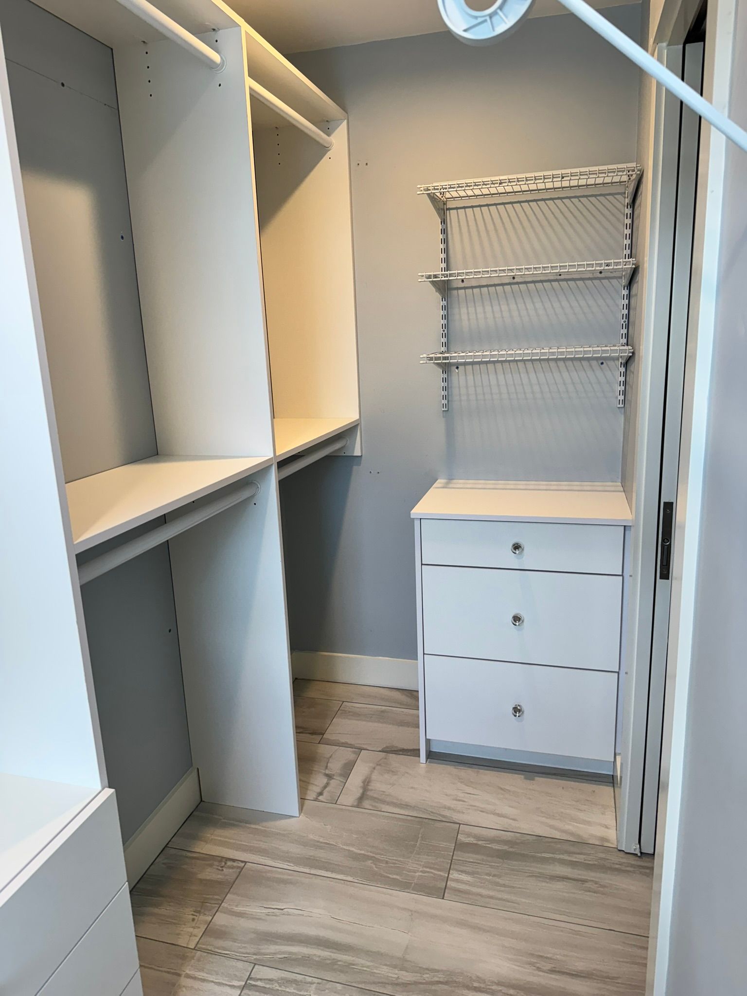 Walk-in closet with white shelving, hanging rods, drawers, and light wood flooring.