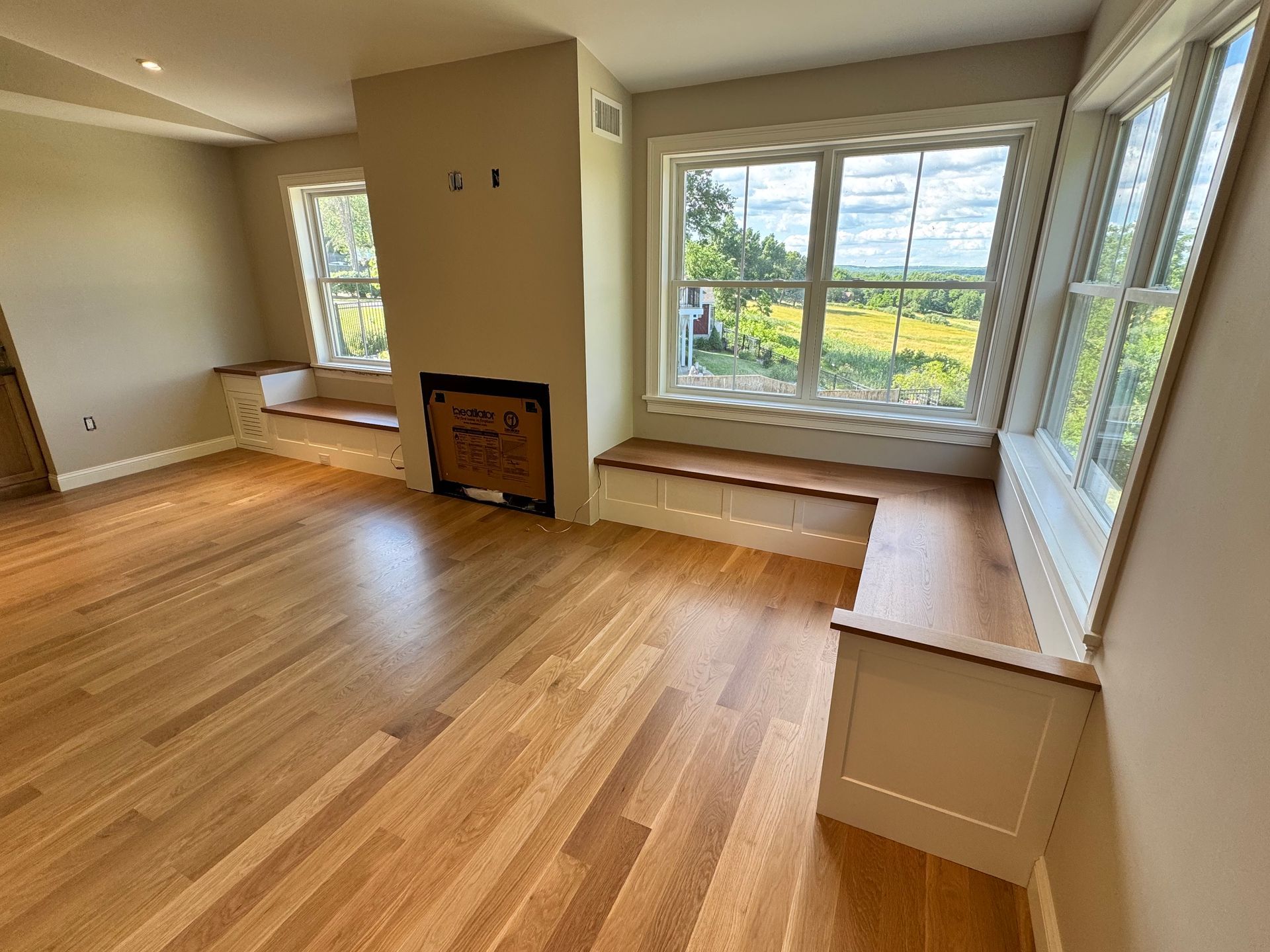 Empty living room with hardwood floors, large windows, and built-in window bench seats.