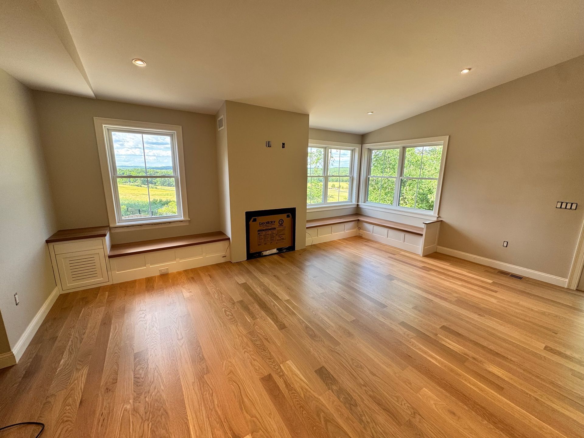 Empty living room with hardwood floors, beige walls, windows, and built-in bench seating