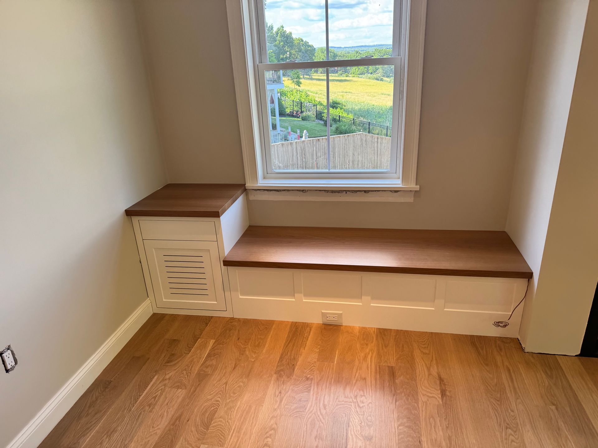 Small room with wood floor, window seat bench, and built-in storage under a window.