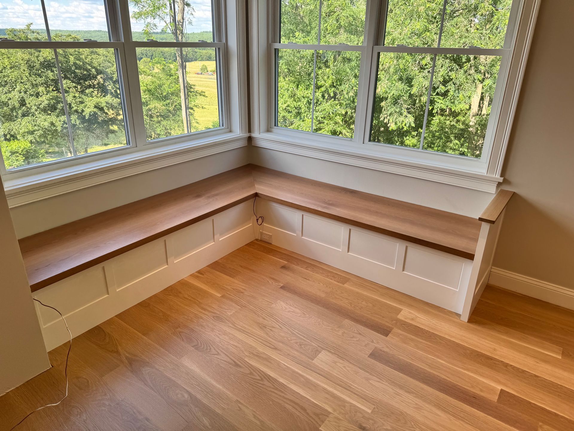 Built-in window seat with white storage cabinets in a sunlit corner room with hardwood floors