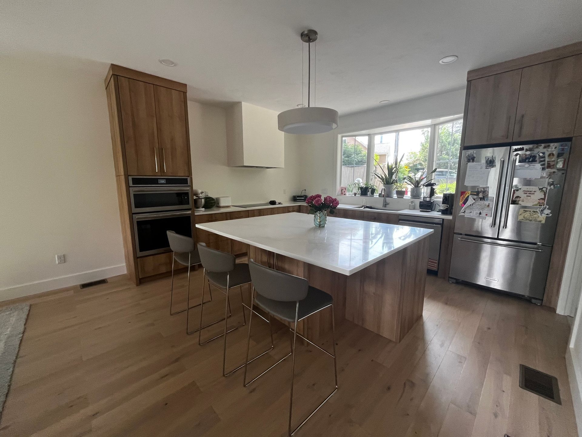 Modern kitchen with island, bar stools, wood cabinets, stainless fridge, and bright window.