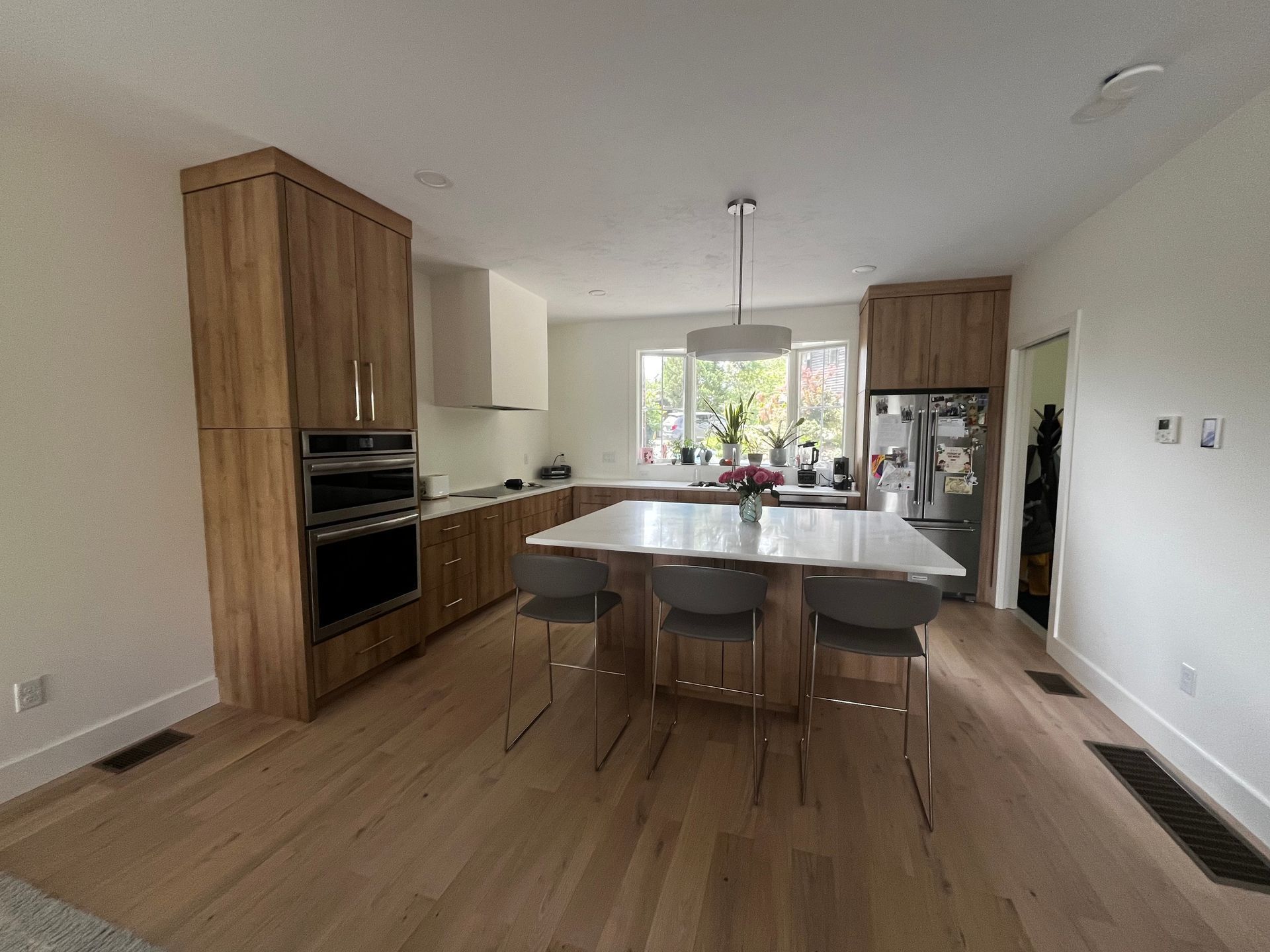 Modern kitchen with island, bar stools, wooden cabinets, stainless fridge, and large window over sink