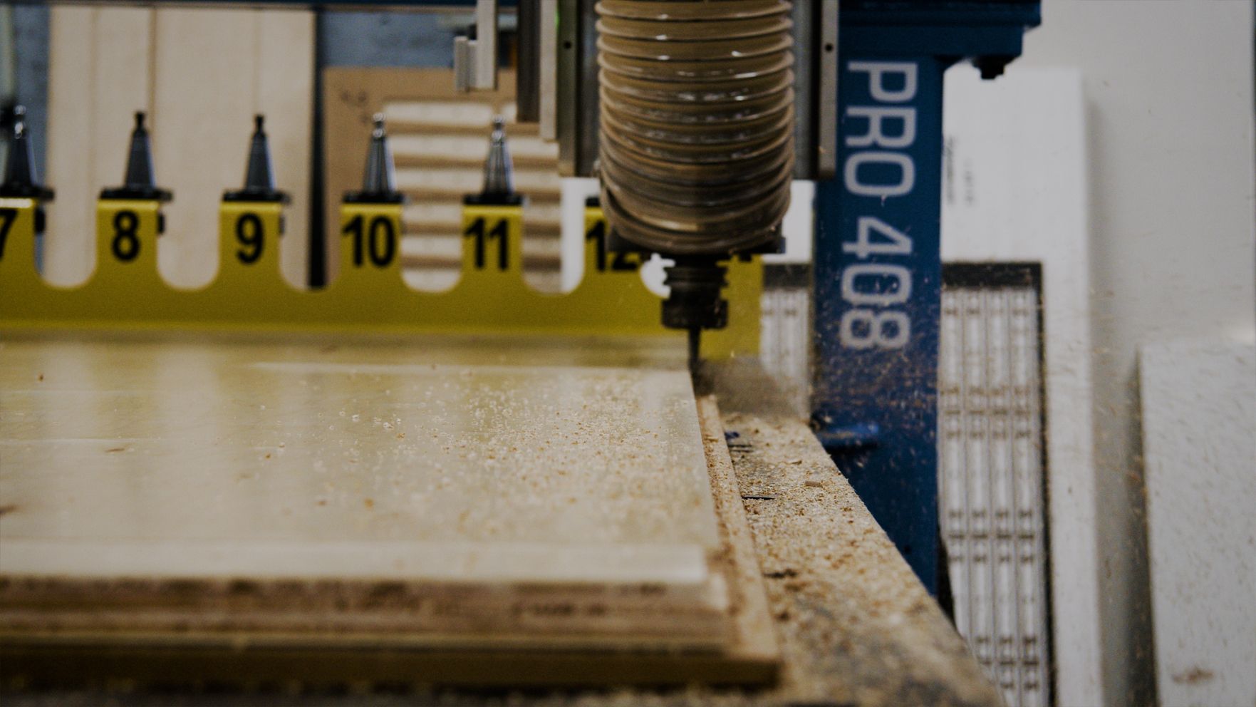 CNC router cutting a wood panel, sawdust visible.