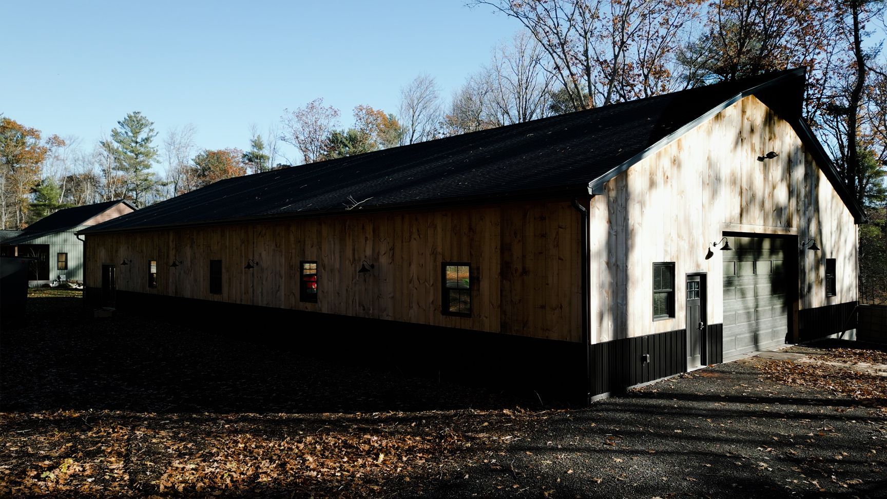 Long wooden barn with a dark roof and large door in an outdoor setting.