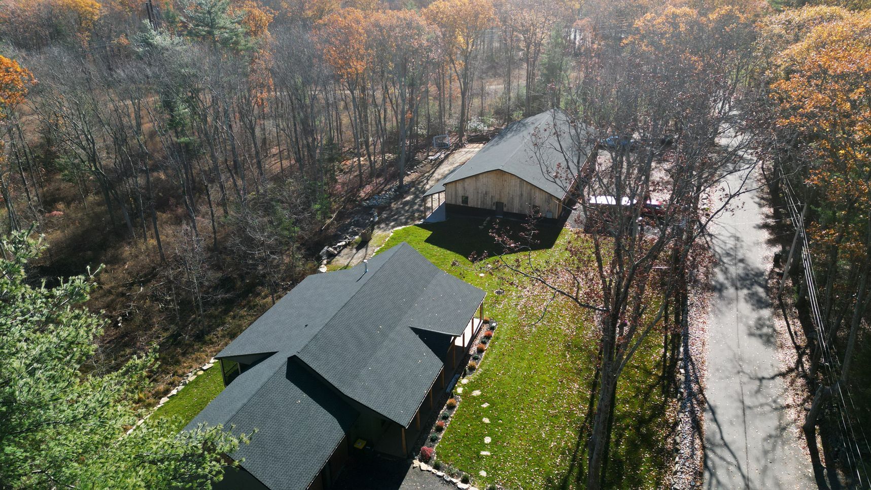 Aerial view of two homes with dark roofs, surrounded by trees with fall foliage.