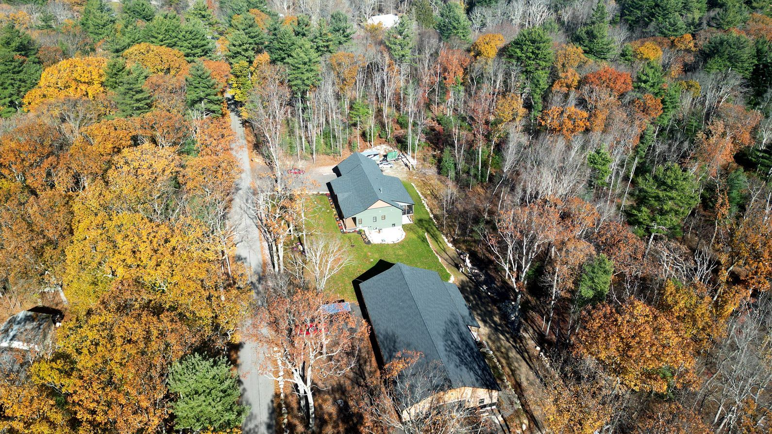 Aerial view of two houses with dark roofs surrounded by autumn trees.